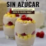 Vasos con capas de arroz con leche cremoso, frambuesas y trozos de mango. En el fondo, un frasco con arroz y una jarra con leche.