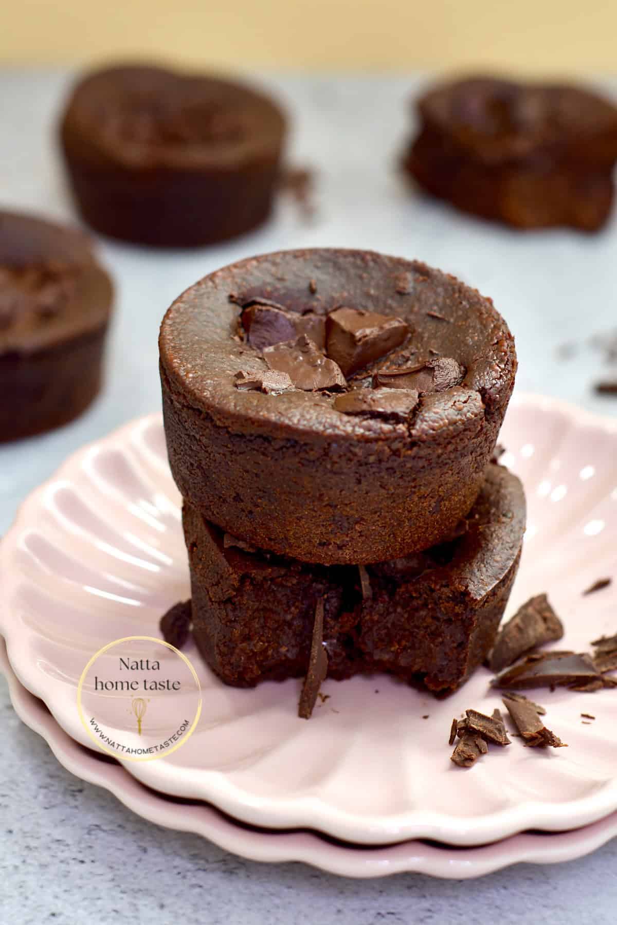 Brownies sin huevo caseros, servidos en un plato rosa. Están hechos con frijoles negros y avena, y decorados con trozos de chocolate derretido. Uno de los brownies está partido, mostrando su interior húmedo y chocolatoso.