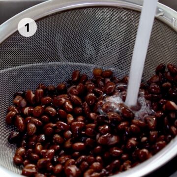 Frijoles negros en un colador siendo enjuagados bajo el chorro de agua, primer paso para preparar brownies sin huevo.