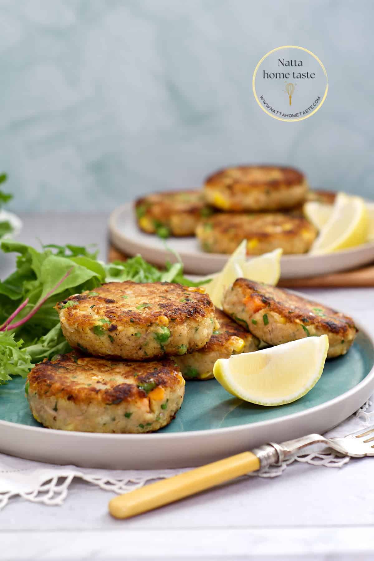 Tortitas de atún con papa doradas por fuera y suaves por dentro, servidas con gajos de limón y hojas verdes.