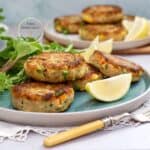 Tortitas de atún con papa doradas por fuera y suaves por dentro, servidas con gajos de limón y hojas verdes.