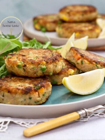 Tortitas de atún con papa doradas por fuera y suaves por dentro, servidas con gajos de limón y hojas verdes.