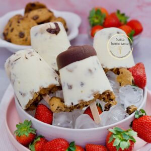 Paletas cremosas de leche con galletas y chocolate, servidas sobre hielo en un bowl rosado con fresas frescas. Receta casera de Natta Home Taste, ideal para el verano o para vender.
