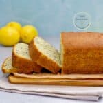 Torta de limón y semillas de amapola recién horneada, cortada en rebanadas y servida sobre una tabla de madera con limones al fondo