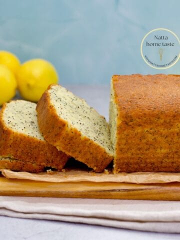 Torta de limón y semillas de amapola recién horneada, cortada en rebanadas y servida sobre una tabla de madera con limones al fondo