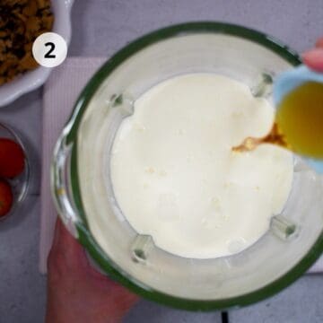Vista superior de una licuadora con mezcla de leche, crema y azúcar mientras se añade extracto de vainilla.