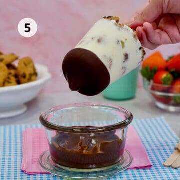 Paleta casera de leche con trozos de galleta, parcialmente sumergida en chocolate derretido.