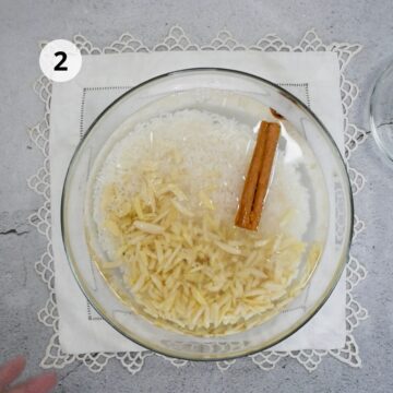 Arroz crudo, almendras laminadas y una rama de canela en remojo dentro de un bol de vidrio con agua.