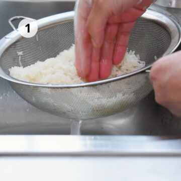 Persona lavando arroz crudo bajo el grifo en un colador de malla metálica.