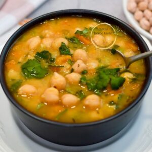 Sopa de garbanzos casera y cremosa en tazón negro, con cilantro, zanahoria y caldo dorado; lista para servir, vista de cerca.