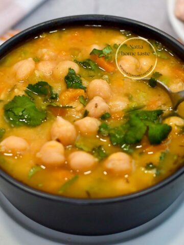 Sopa de garbanzos casera y cremosa en tazón negro, con cilantro, zanahoria y caldo dorado; lista para servir, vista de cerca.