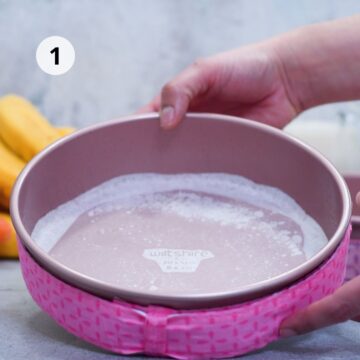 Molde redondo de 20 cm preparado con papel y harina, rodeado por banda para hornear rosa; manos sosteniéndolo para un horneado parejo.