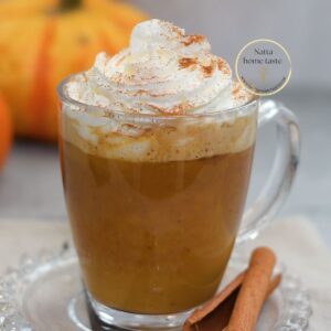 Pumpkin Spice Latte casero servido en taza de vidrio con crema batida y canela espolvoreada, una bebida de café con calabaza y especias perfecta para el otoño.