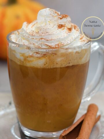 Pumpkin Spice Latte casero servido en taza de vidrio con crema batida y canela espolvoreada, una bebida de café con calabaza y especias perfecta para el otoño.