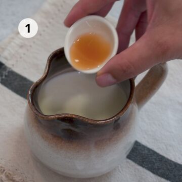 Mano vertiendo vinagre de manzana en una jarra con leche para comenzar la preparación de la masa.