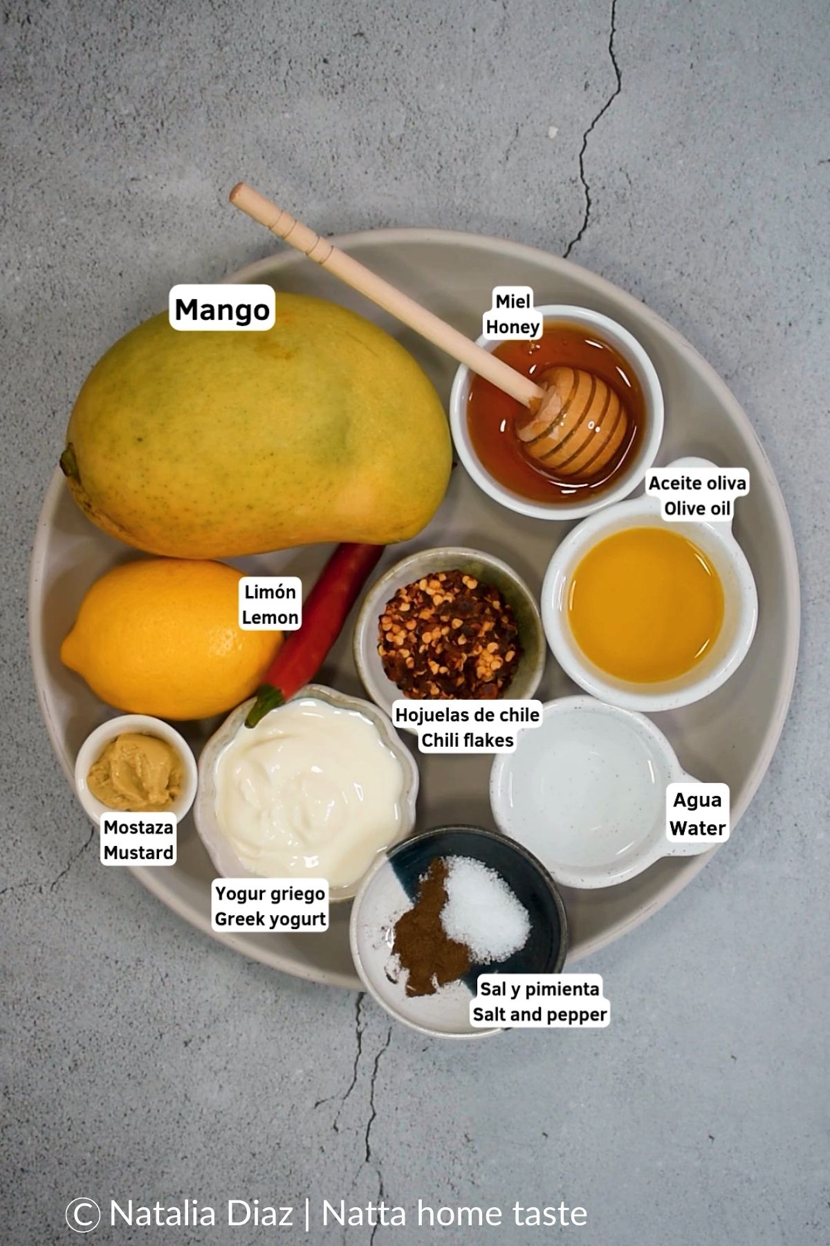 Plato con los ingredientes para una vinagreta de mango casera, incluyendo mango fresco, limón, miel, aceite de oliva, yogur griego, mostaza y hojuelas de chile.