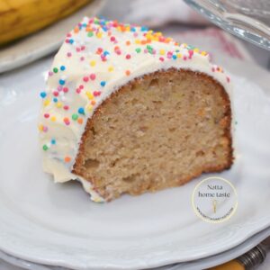 Rebanada de torta de cumpleaños de banana con crema de mantequilla y grageas de colores, mostrando su miga húmeda y suave.