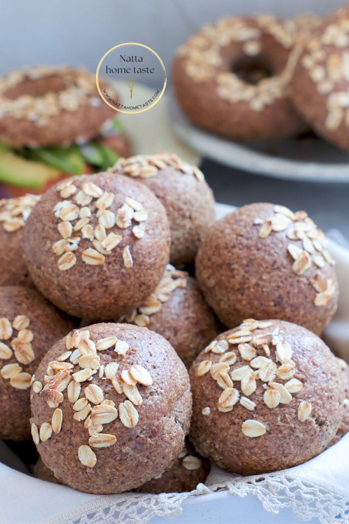 Rollitos de pan de avena sin huevo decorados con hojuelas, con panes tipo bagel y un sándwich al fondo.