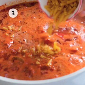 Pasta pequeña agregándose al caldo de tomate mientras hierve en la olla.