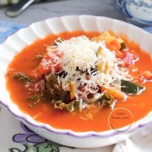 Sopa minestrone vegetariana con pasta, frijoles, calabacín y kale, servida con queso parmesano rallado.