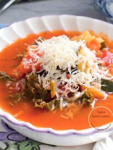 Sopa minestrone vegetariana con pasta, frijoles, calabacín y kale, servida con queso parmesano rallado.